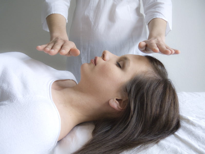 Sesión de Reiki: la terapeuta acerca las manos a la cabeza de la persona recostada